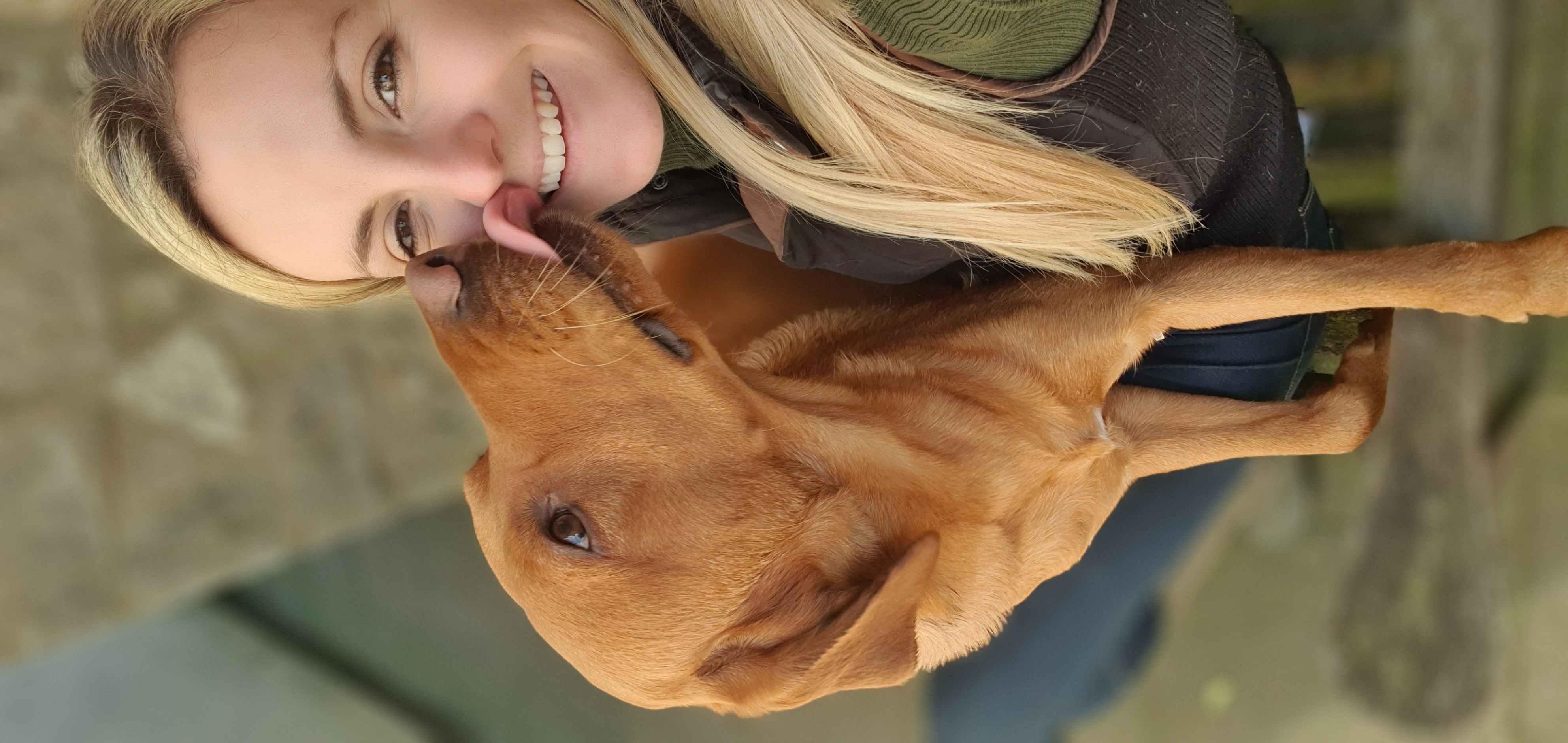 Libbie, the groomer, smiling beside a brown dog outdoors